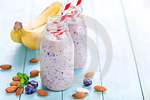 Banana and blueberry diet smoothie with yogurt or milk, almonds and fresh berries in glass bottles