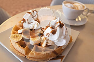 Banana, caramel and whipped ice cream waffle with a wafer next to a n espresso coffee with ice-cream in a cup and saucer