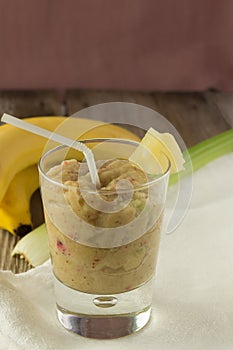 Banana and celery smoothie with berries on wooden table vertical