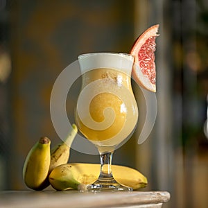Banana and citrus smoothie drink. Goblet or Glass with mixed shaked fruits on blurred background. Refreshing detox photo