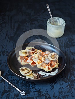 Banana curd waffles on a black plate with honey in a glass jar and a spoon