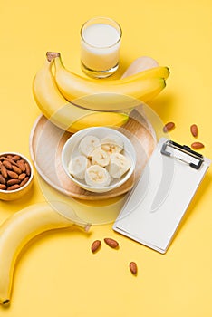 Banana and milk on yellow paper background with blank clipboard