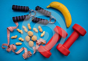 Banana, nuts, measuring tape, hand grip strengthener and dumbbells on a blue background