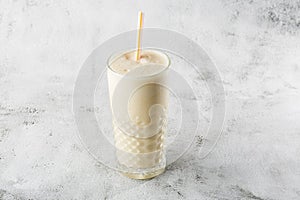 Banana oats smoothie or vanilla milkshake in glass on bright marble background. Overhead view, copy space. Advertising for