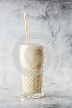 Banana oats smoothie or vanilla milkshake in glass on bright marble background. Overhead view, copy space. Advertising for