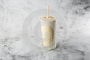 Banana oats smoothie or vanilla milkshake in glass on bright marble background. Overhead view, copy space. Advertising for