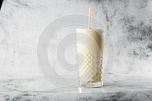 Banana oats smoothie or vanilla milkshake in glass on bright marble background. Overhead view, copy space. Advertising for