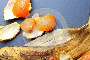 Banana and orange peels on grey background, close up