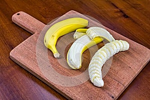 Banana, peeled banana and sliced banana on a wooden cutting board in angled view