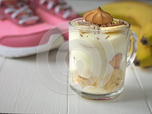 Banana pudding in glass mugs with biscuits and sneakers in the background on a white floor. Milk and banana dessert.