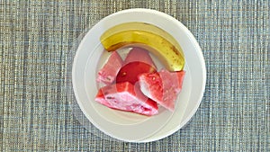 Banana and sliced watermelon on a rotating plate. Rotating fruit plate, top view