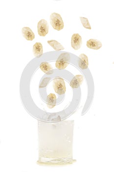 Banana slices falling into a glass of banana milkshake on white