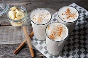 Banana smothie or milkshake with cinnamon on wood background