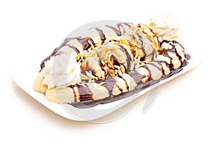 Banana split ice cream sundae on plate with almonds, whipped cream and chocolate topping on white background