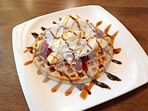 Banana split with whip cream, ice cream, strawberry jam and syrup on top of waffle