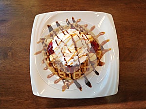 Banana split with whip cream, ice cream, strawberry jam and syrup on top of waffle