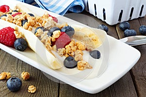 Banana split with yogurt, berries and granola, close up on wood