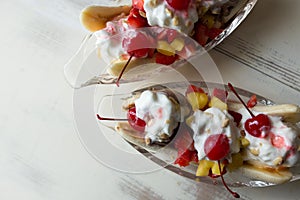 Banana splits with maraschino cherries and melting whipped cream on a vintage table, close up view. Room for copy.