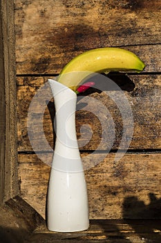 A banana, a white vase, a chili pepper