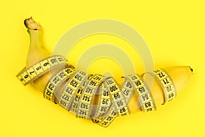 Banana wrapped with a tape measure on a yellow background, a concept of weight loss, healthy nutrition