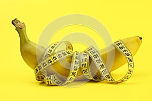 Banana wrapped with a tape measure on a yellow background, a concept of weight loss, healthy nutrition