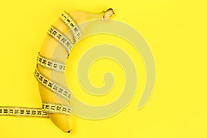 Banana wrapped with a tape measure on a yellow background, a concept of weight loss, healthy nutrition. Copy space