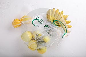 Bananas, apples and lemons in textile grocery mesh bags. Yellow fruits and vegetables in reusable eco friendly packaging on white