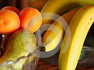 Bananas apricots and a pear in glass bowl