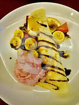 Bananas ice cream crepe roll with whipping cream and strawberry chocolate topping dish