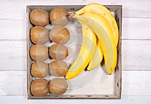 Bananas and kiwis placed in an old wooden tray on a background of old wooden floor