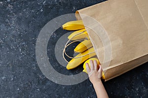 Bananas and lemons in a brown paper bag with hand on a black background. Healthy vegan vegetarian copy space  banner. Shopping