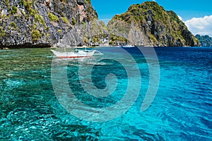 Banca boat moored und crystal clear ocean water near Matinloc island, highlights of hopping trip Tour C. Most beautiful place at