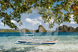 Banca boat in shallow blue water on Ipil beach of Pinagbuyutan Island, El Nido, Palawan, Philippines