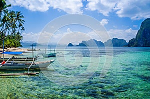 Banca boats in clear water at sandy beach in El Nido, Philippines