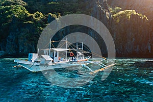 Banca local boat on turquoise water against huge limestone cliffs. Island hopping tour trip. Exploring Philippines