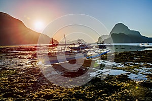 Banca local boats during low tide. Sunrise and amazing shape of rocks of Cadlao Island in background, El-Nido, Palawan