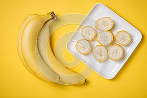 A banch of bananas and a sliced banana in a dish over yellow background.