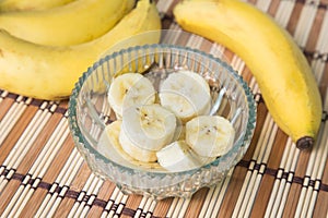 A banch of bananas and a sliced banana in a pot over a wood background