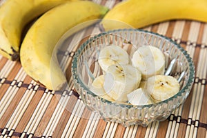 A banch of bananas and a sliced banana in a pot over a wood background