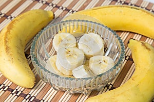 A banch of bananas and a sliced banana in a pot over a wood background