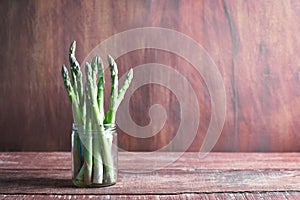 Banches of fresh green asparagus in a jar on wooden background