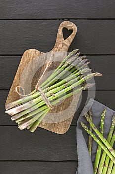 banches of fresh green asparagus on wooden background, top view, vertical photo