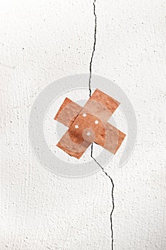 Band-aid plaster in cross shape on a crack in the wall, concept