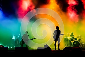 A band of three musicians playing instruments in front of a colorful smoke backdrop.