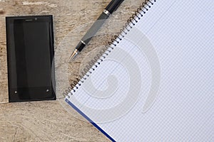 Banded notebook, cell phone and pen on a wooden table with copyspace