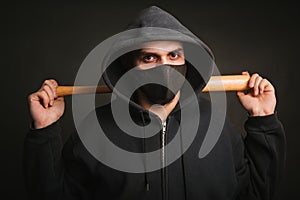 Bandit in a black sweatshirt and a medical mask. Dangerous man with a baseball bat ready to fight