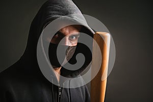 Bandit in a black sweatshirt and a medical mask. Dangerous man with a baseball bat ready to fight