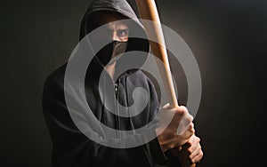 Bandit in a black sweatshirt and a medical mask. Dangerous man with a baseball bat ready to fight