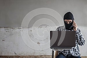 The bandit hacking the data in laptop and talking on smartphone for ransom