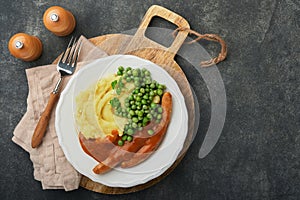 Bangers and mash. Grilled sausages with mash potato and green pea on white plate on black dark background. Traditional dish of
